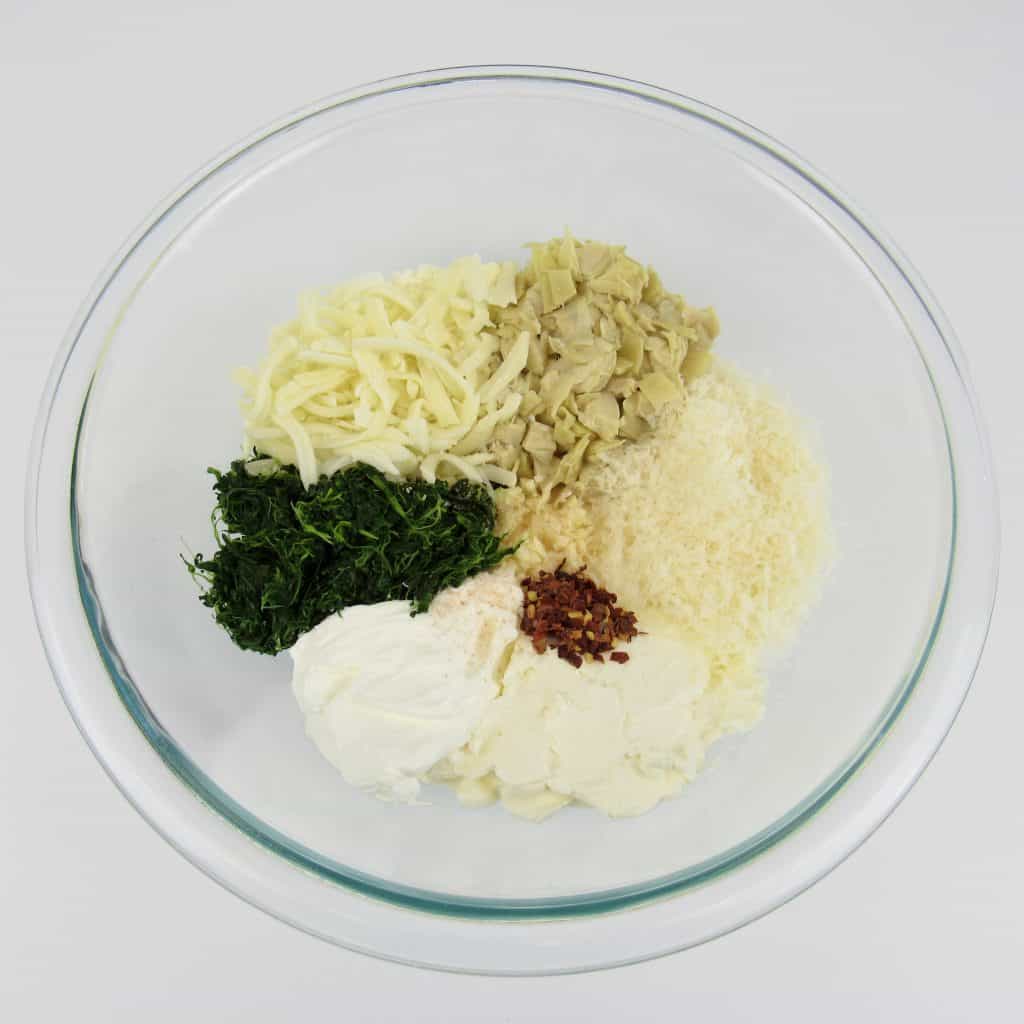 spinach artichoke filling ingredients unmixed in glass bowl
