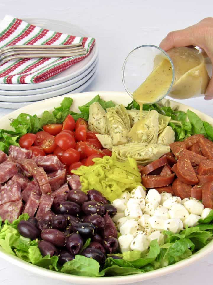 antipasto salad in white bowl with dressing being poured on top