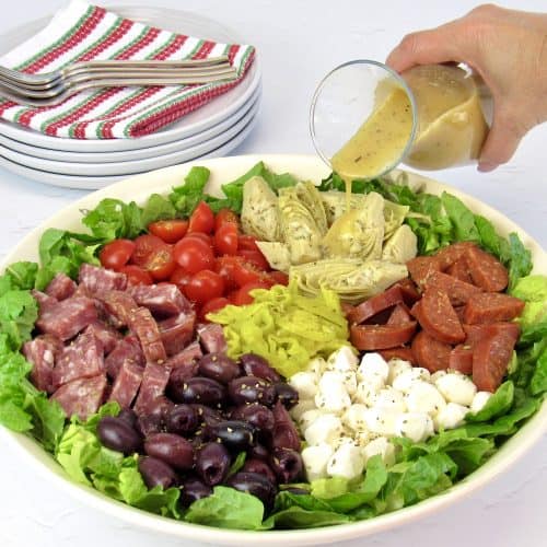 antipasto salad in white bowl with dressing being poured on top