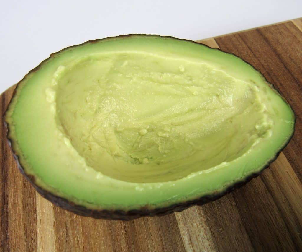 half an avocado on cutting board with pit removed