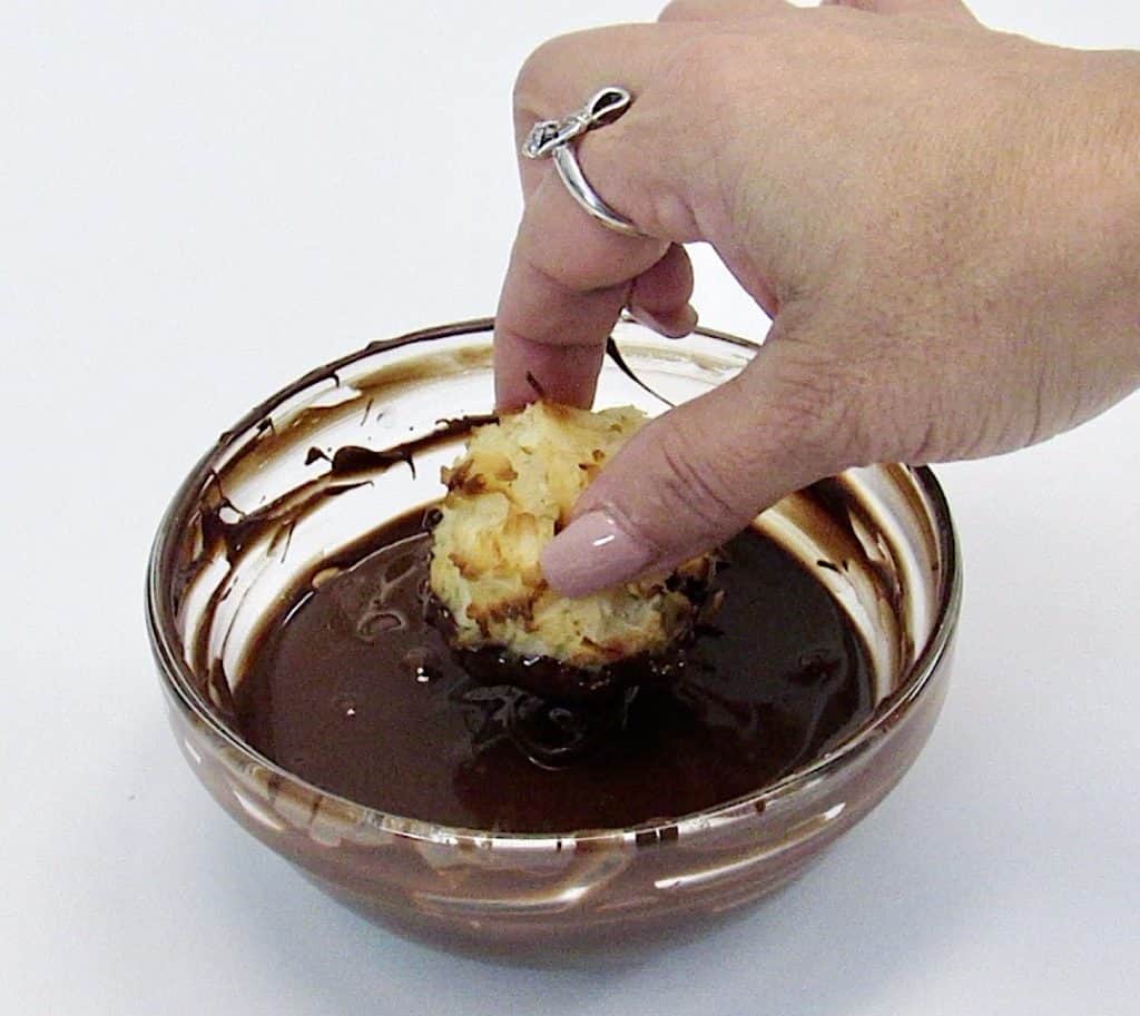 coconut macaroon being dipped in bowl of chocolate