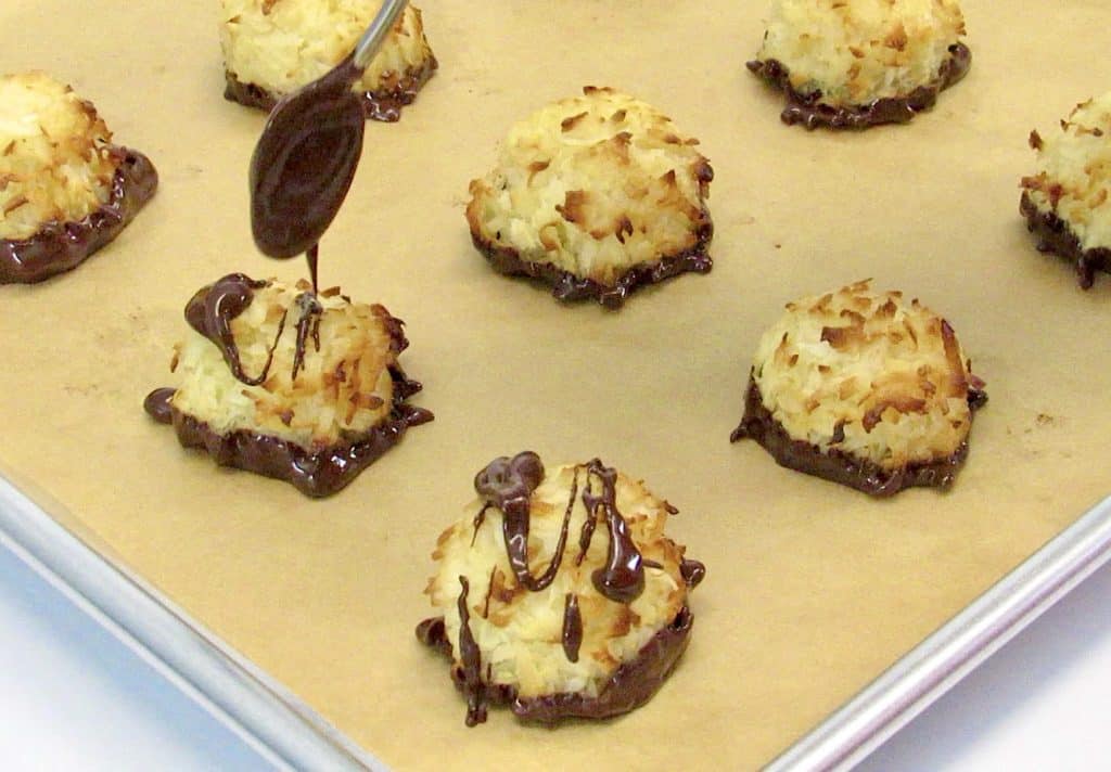 coconut macaroons on baking sheet with chocolate being drizzled on top
