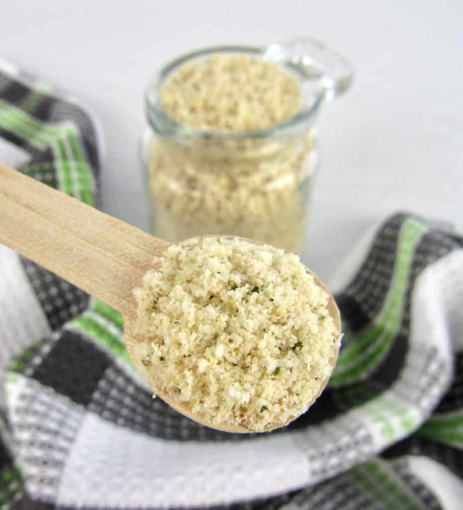 Keto Bread Crumbs in glass jar with wooden spoon holding up some