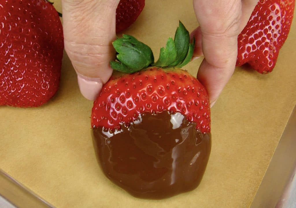 chocolate dipped strawberry being put on parchment paper
