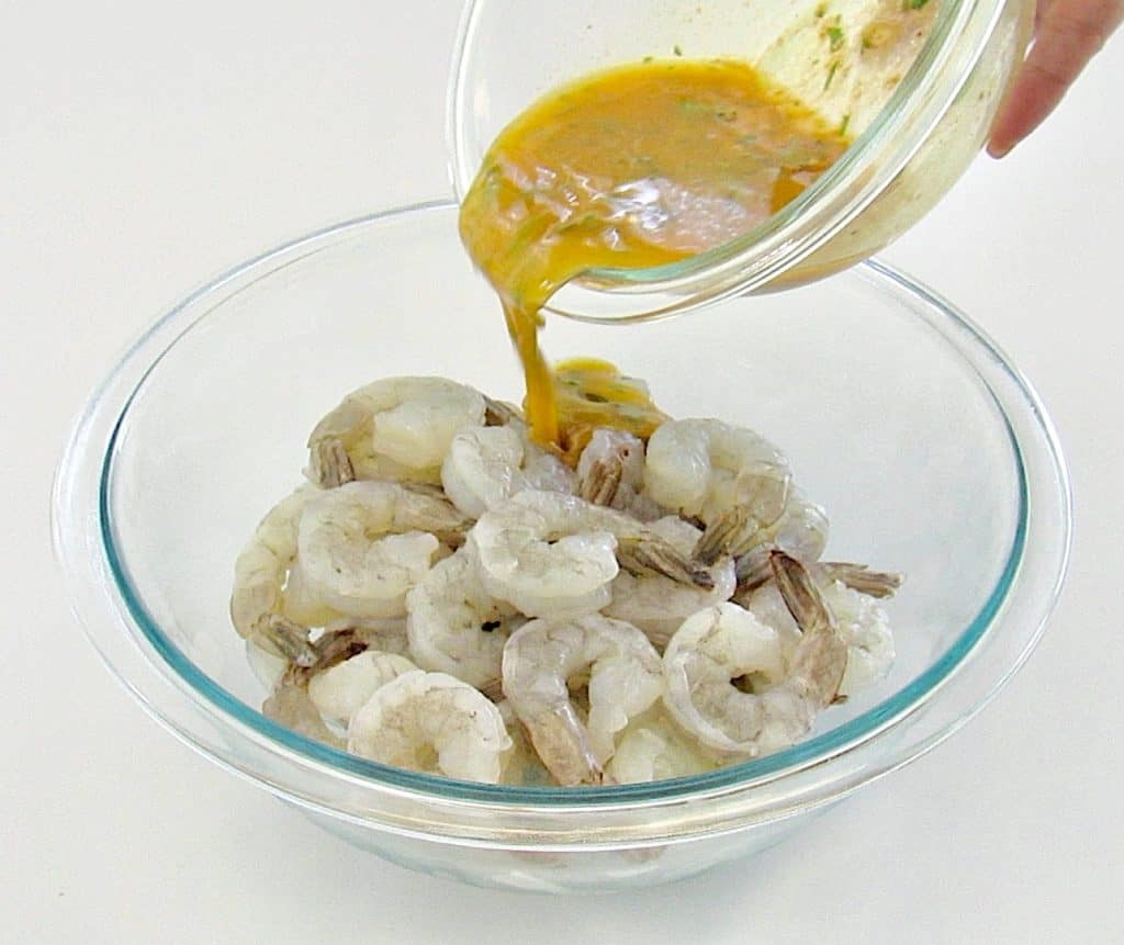garlic butter sauce being poured over raw shrimp in glass bowl