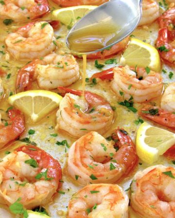baked shrimp on baking sheet with butter being spooned over