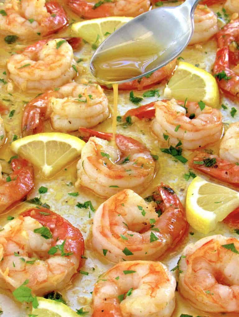 baked shrimp on baking sheet with butter being spooned over