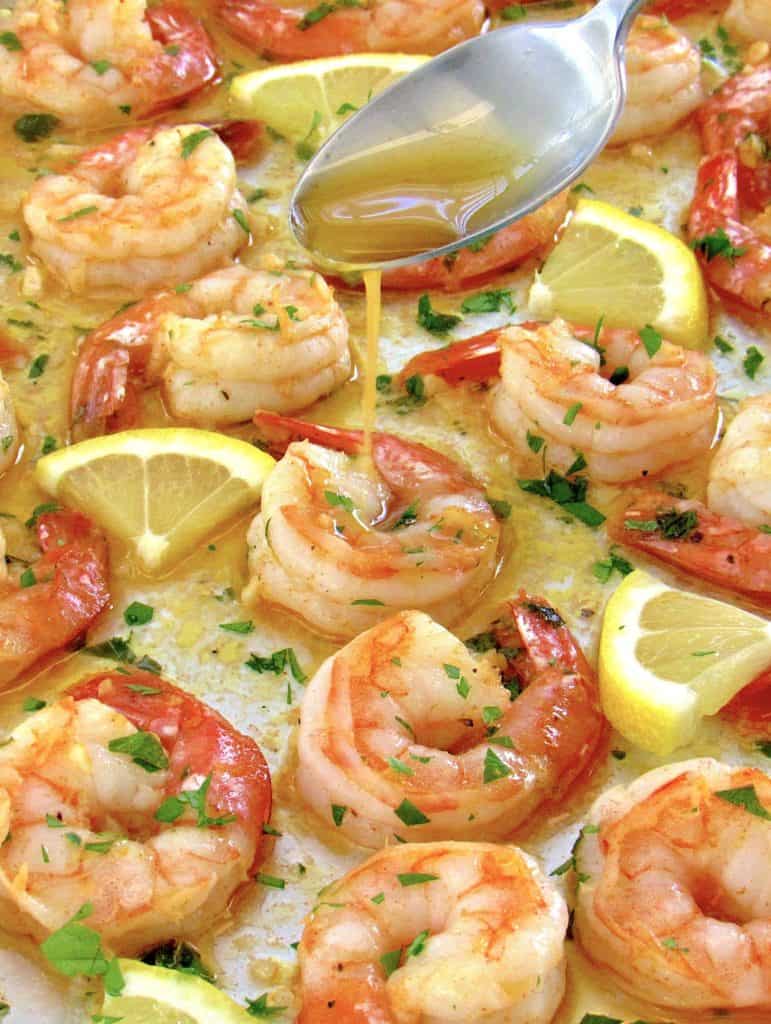 baked shrimp on baking sheet with butter being spooned over