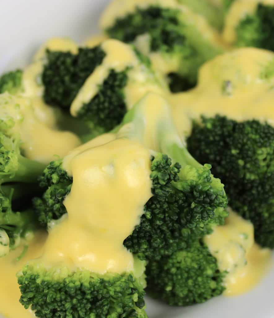 closeup of cheese sauce over broccoli on white plate