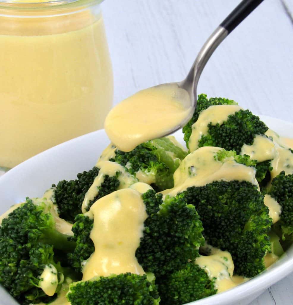 cheese sauce being spooned over broccoli in white dish