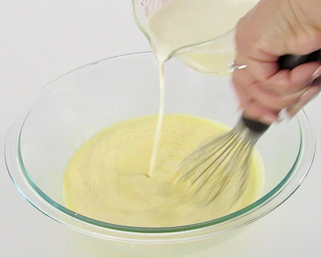 cream being poured over egg mixture being whisked