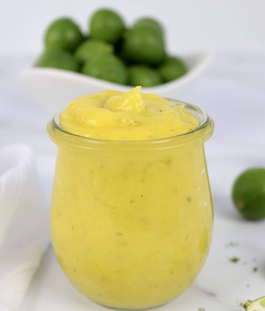 closeup of Keto Key Lime Curd in glass jar with limes in background