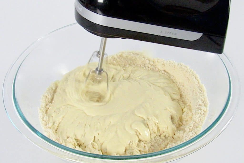wet and dry pound cake ingredients being mixed in glass bowl