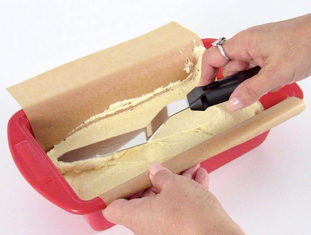 pound cake batter being spread into red loaf pan