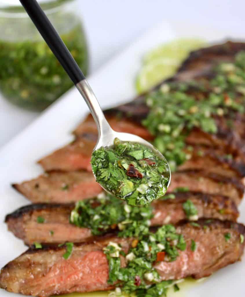 chimichurri sauce being spooned over slicked steak on white plate