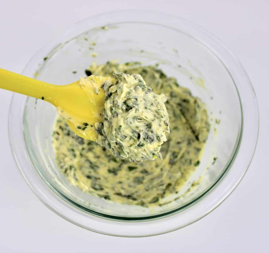 garlic herb compound butter mixture being spooned out with yellow spatula