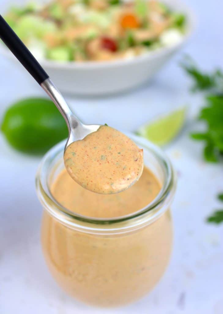 Keto Chipotle Ranch Dressing being spooned out of glass jar with salad in background