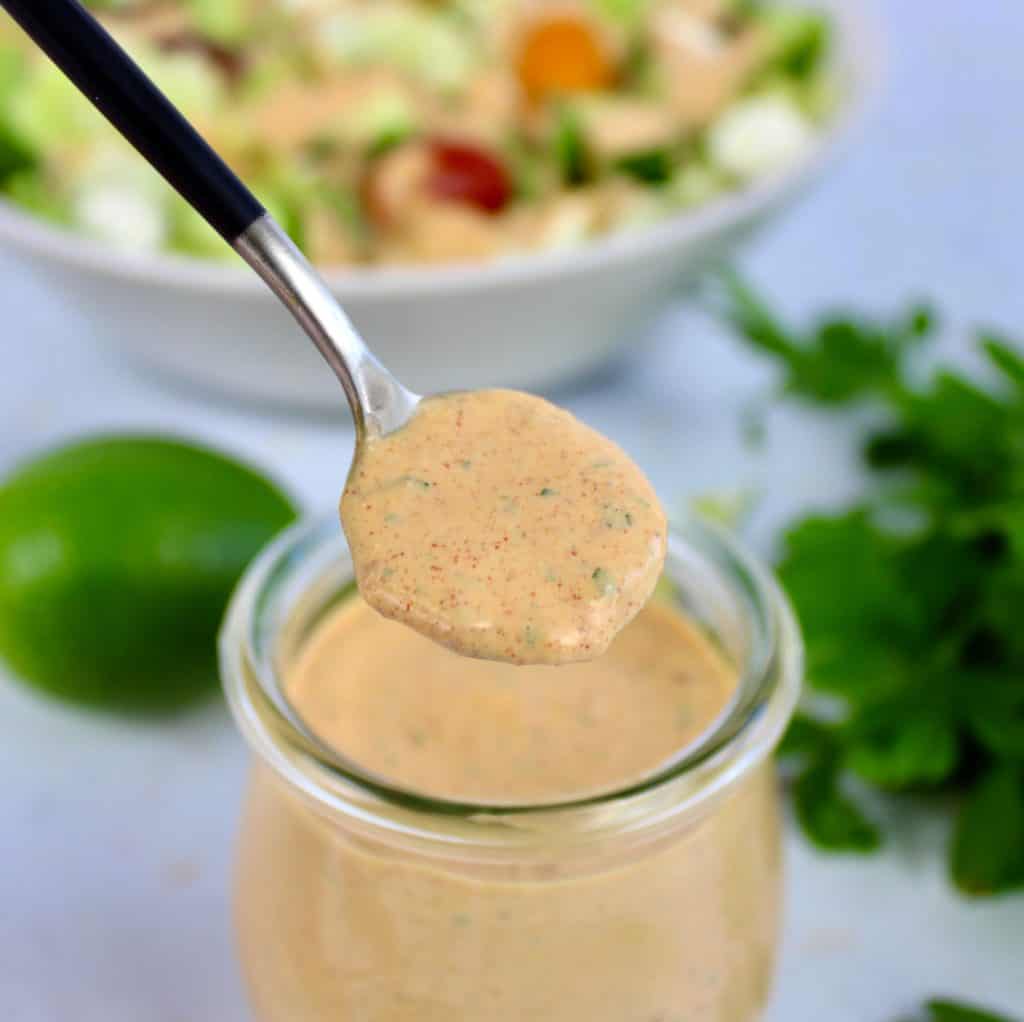 Keto Chipotle Ranch Dressing being spooned out of glass jar with salad in background