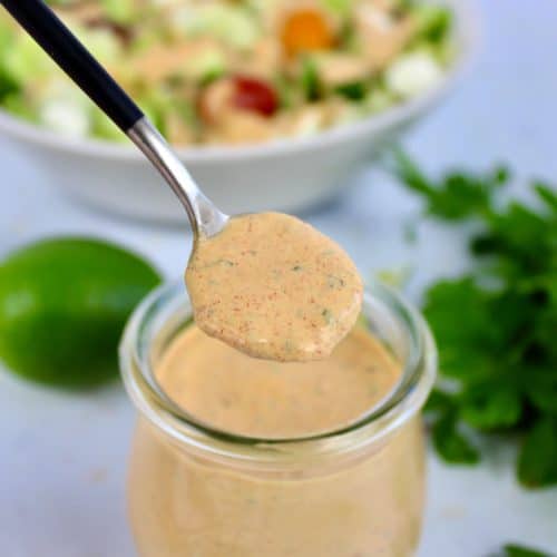 Keto Chipotle Ranch Dressing being spooned out of glass jar with salad in background