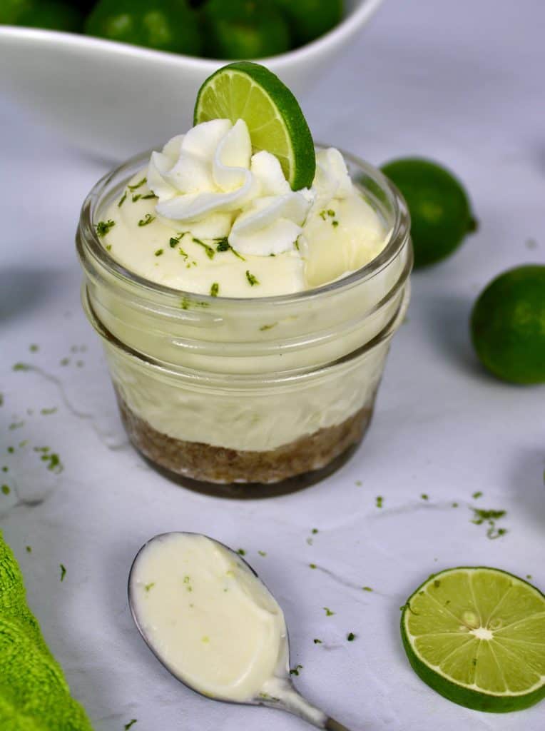 Keto No Bake Key Lime Cheesecake in glass jar with whip cream and lime on top with spoonful on the side