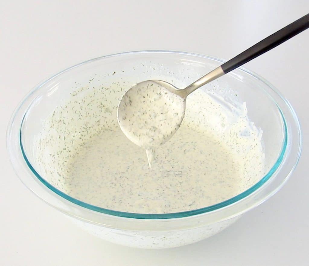 ingredients for ranch dressing in glass bowl with spoon dripping