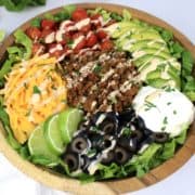 closeup of taco salad in wooden bowl with dressing drizzled on top