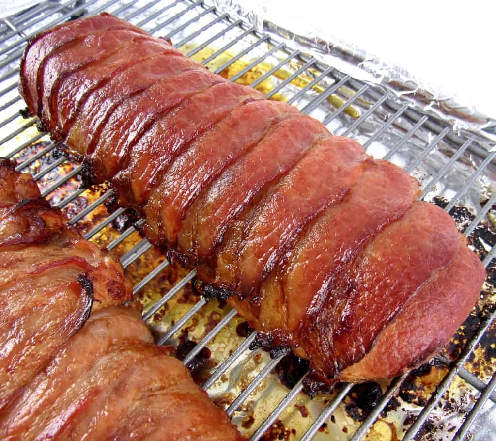 2 cooked pork tenderloins wrapped in bacon on baking rack