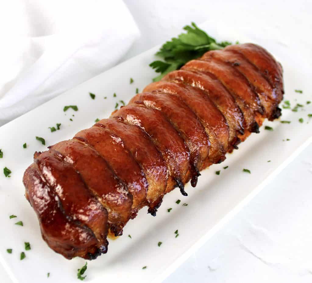 Bacon Wrapped Pork Tenderloin on white plate with parsley