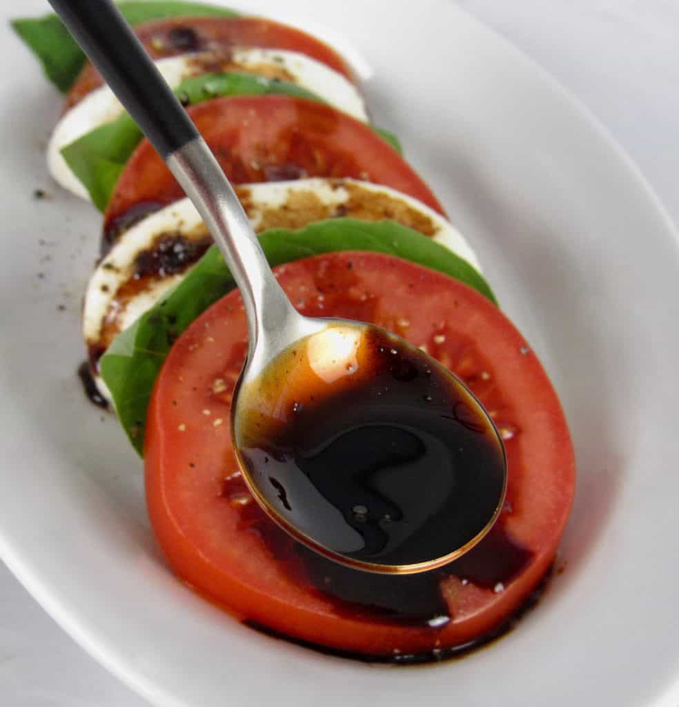 Balsamic Reduction in spoon held over tomato