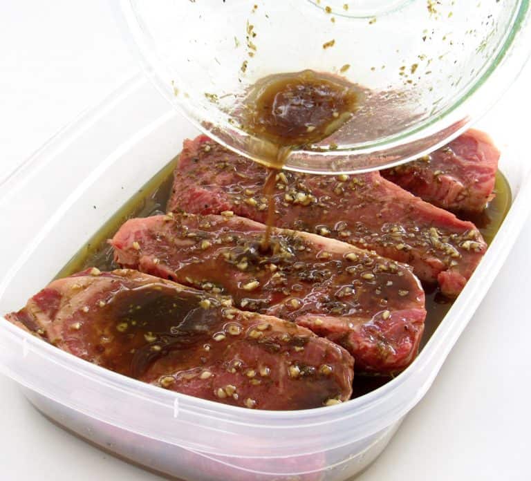 marinade being poured over 4 steaks in tupperware container
