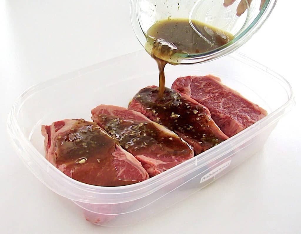 marinade being poured over 4 steaks in tupperware container