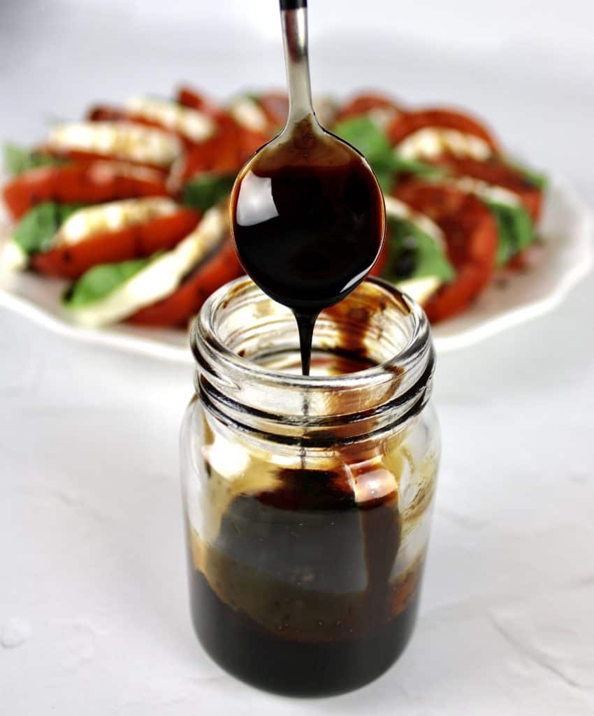 balsamic reduction being spooned out of glass jar with salad in background