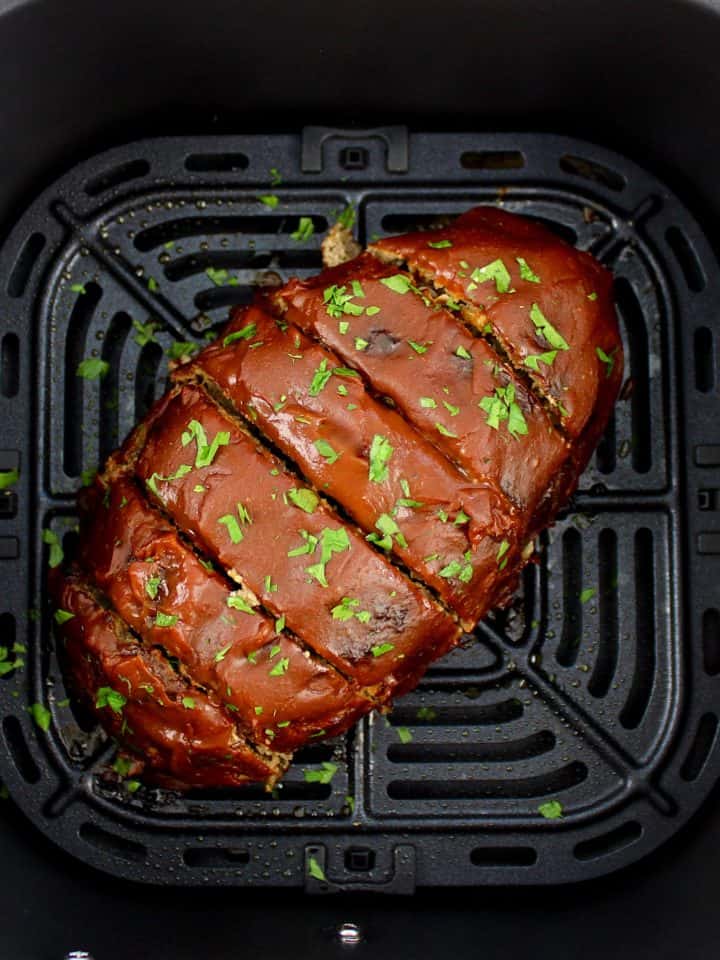 meatloaf with slices in air fryer basket and parsley garnish