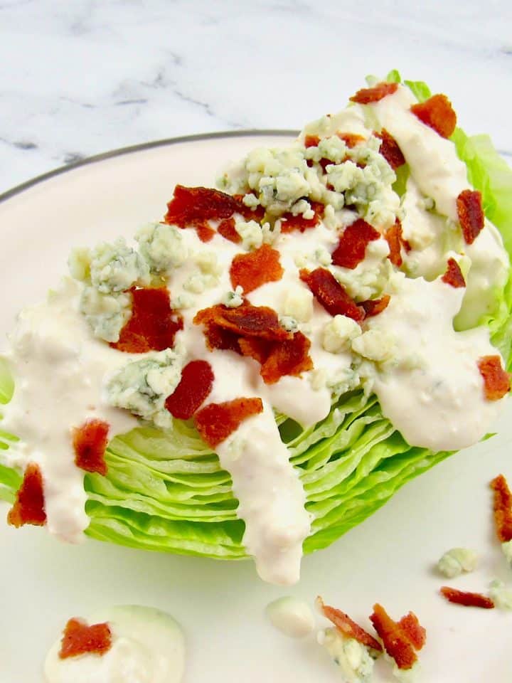 wedge of iceberg lettuce topped with blue cheese dressing, crumbles and bacon
