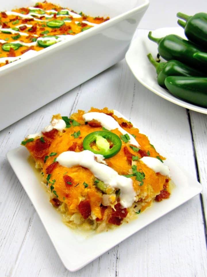 slice of jalapeno popper chicken casserole with casserole and bowl of peppers in background