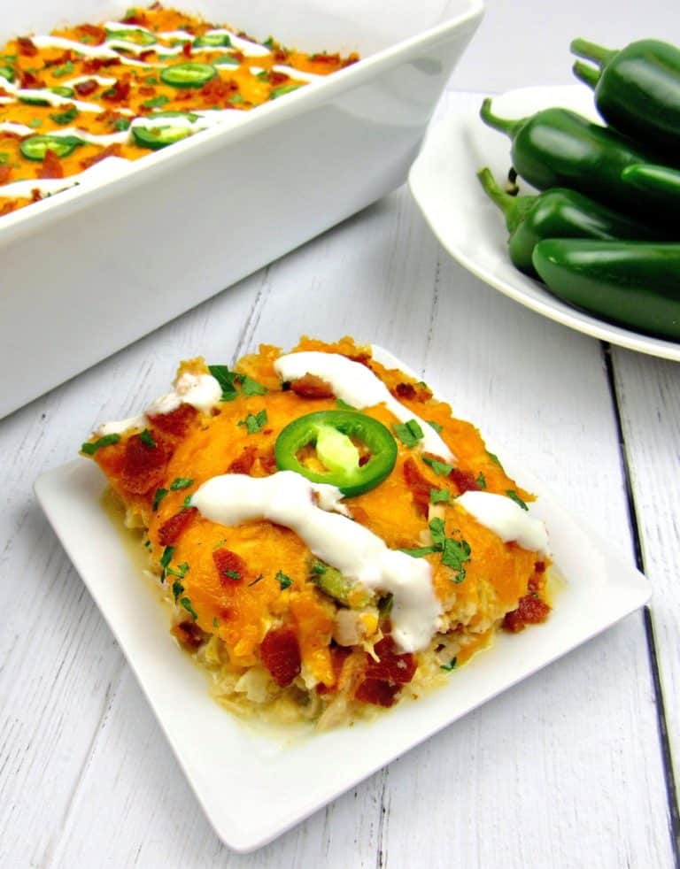 slice of jalapeno popper chicken casserole with casserole and bowl of peppers in background