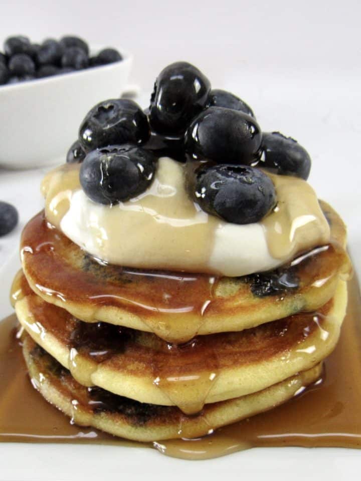closeup of blueberry pancakes with syrup whip cream and blueberries on top