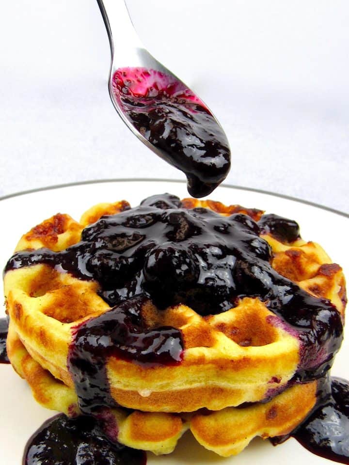 closeup of blueberry sauce in spoon over waffles