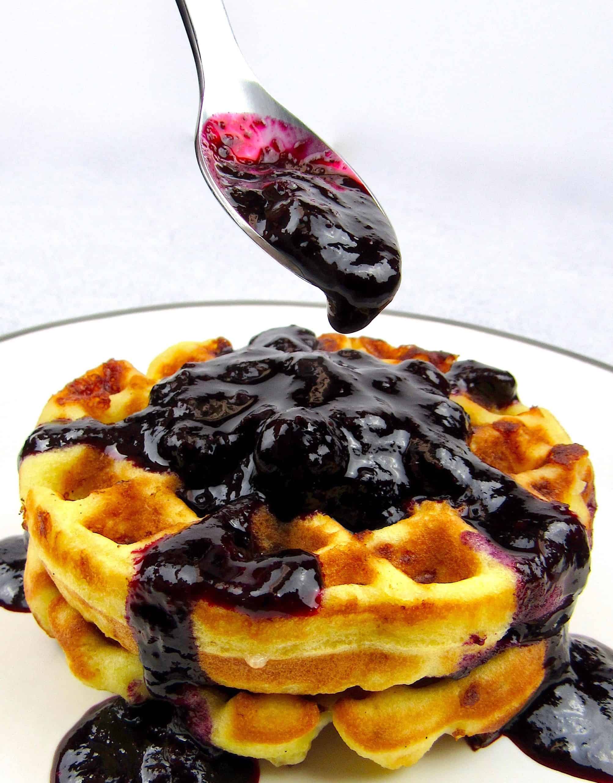 closeup of blueberry sauce in spoon over waffles