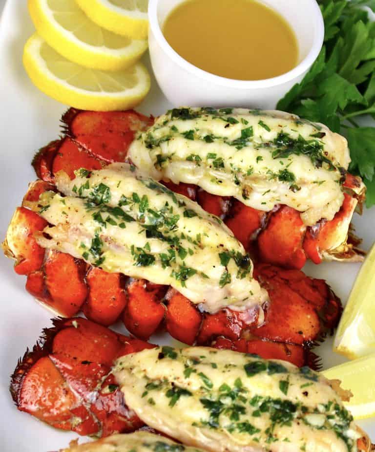 Broiled Lobster on white plate with butter and lemon slices in background