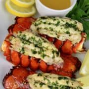 overhead view of 4 lobster tails with butter and lemons on white platter