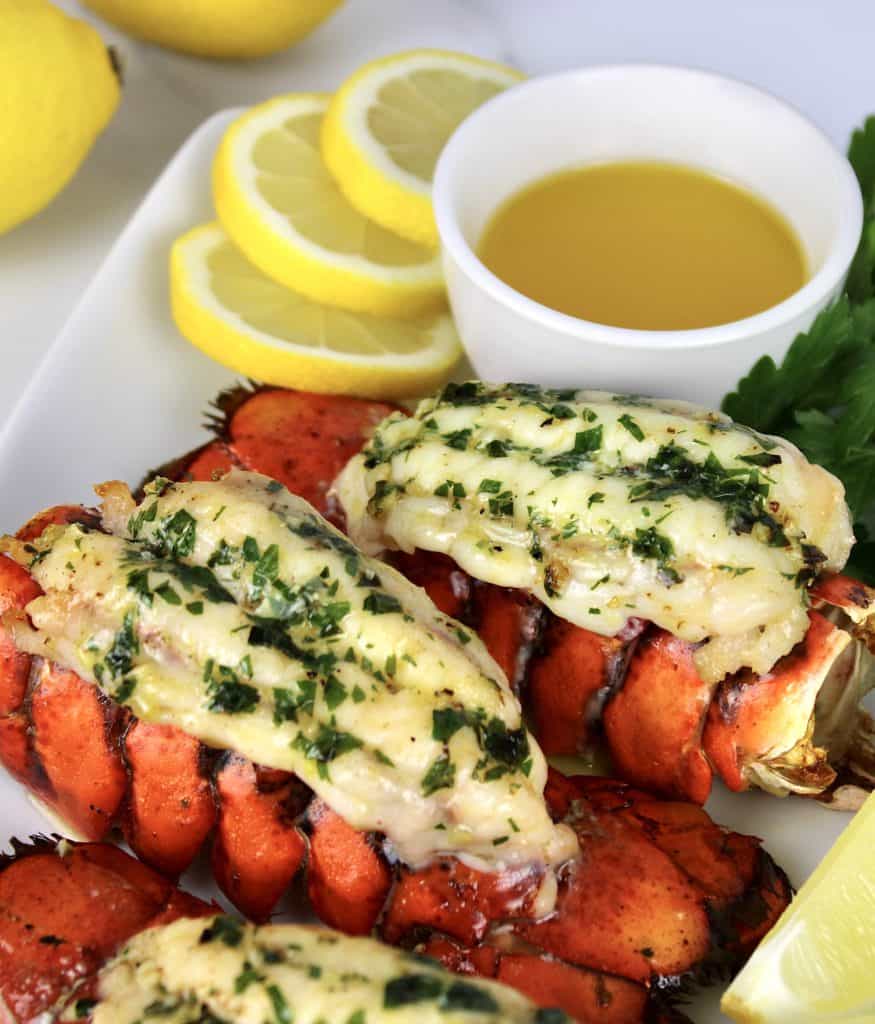 overhead view of 4 lobster tails with butter and lemons on white platter