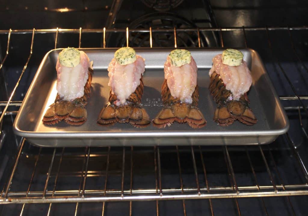 4 lobster tails with compound butter pads on top in the oven
