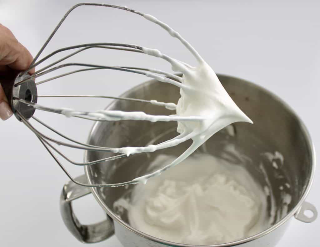 whisk holding up whipped egg whites over stand mixer bowl