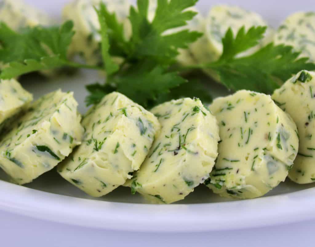closeup of Garlic Herb Compound Butter arranged in a circle on white plate parsley in center