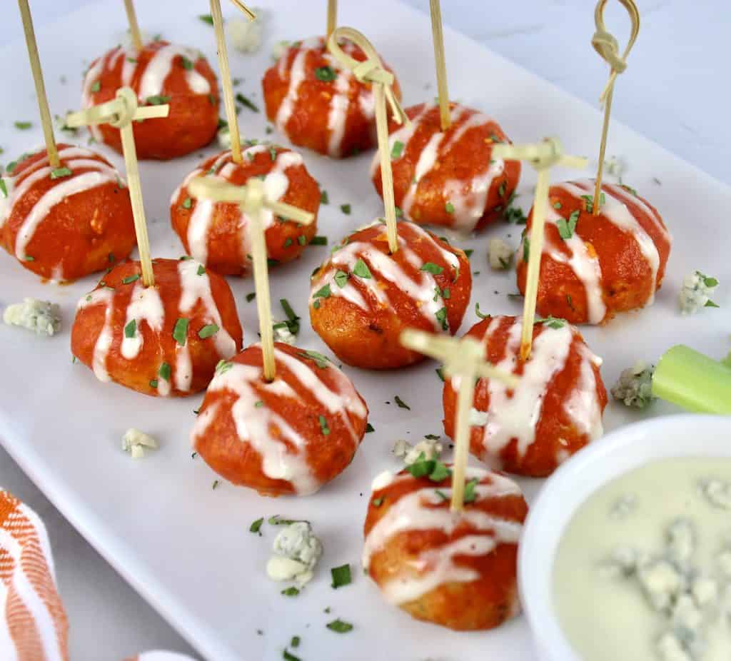 Keto Buffalo Chicken Meatballs on white platter with fancy toothpicks and blue cheese on side