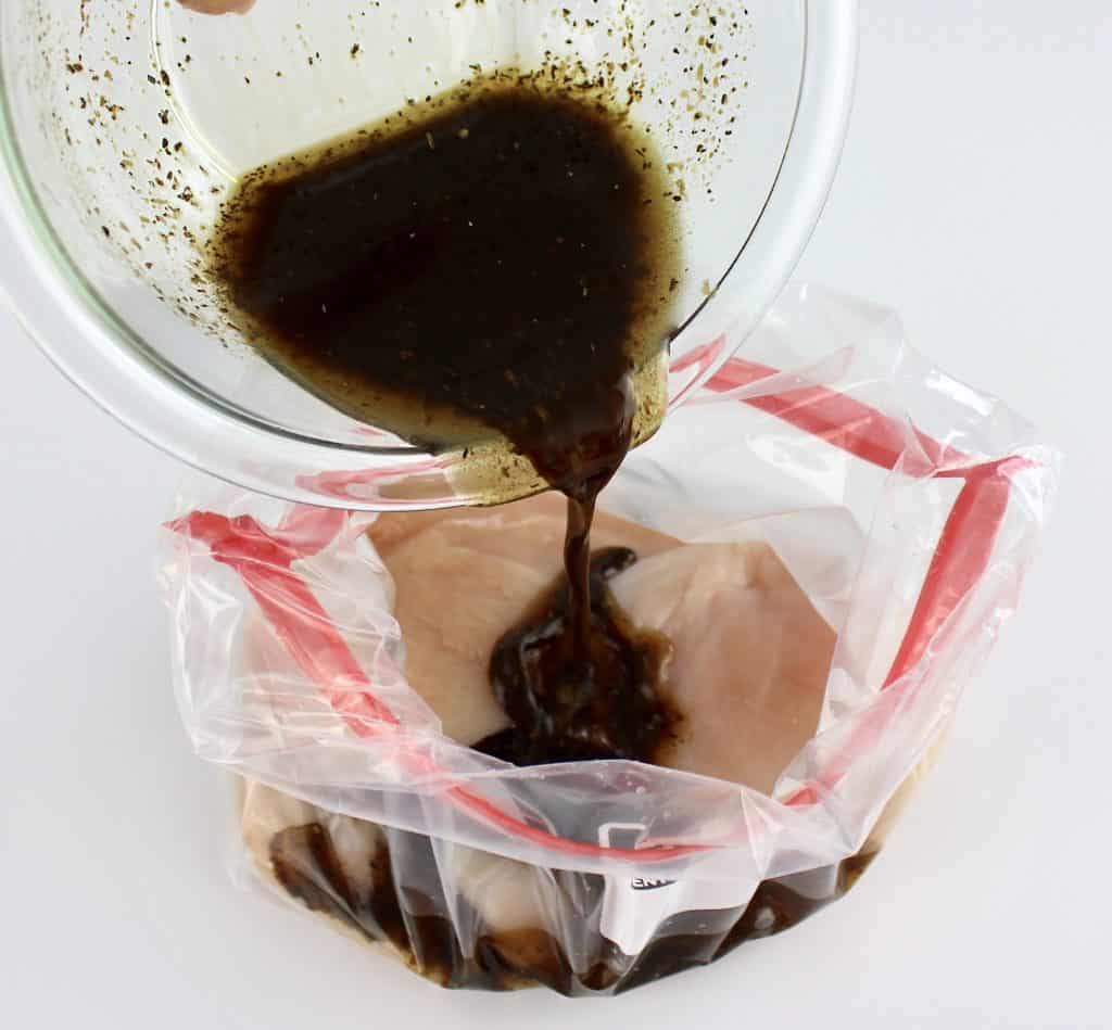 balsamic marinade being poured over chicken in food storage bag