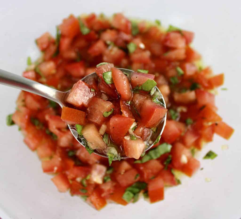 bruschetta in glass bowl with spoon holding up some