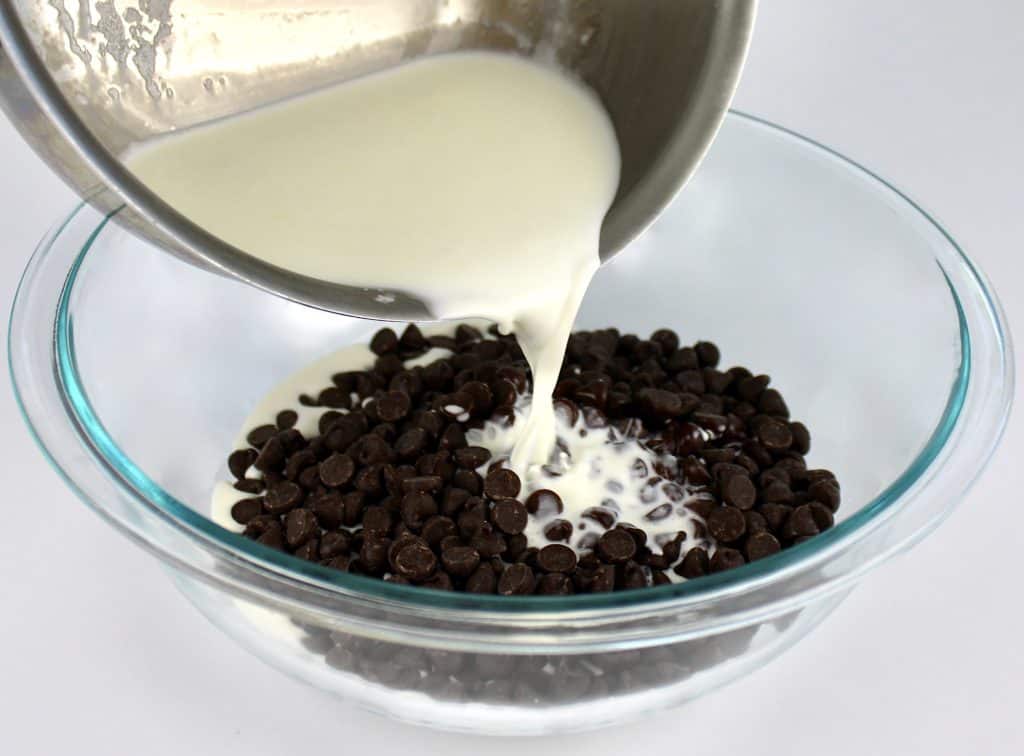 cream being poured over chocolate chips in glass bowl