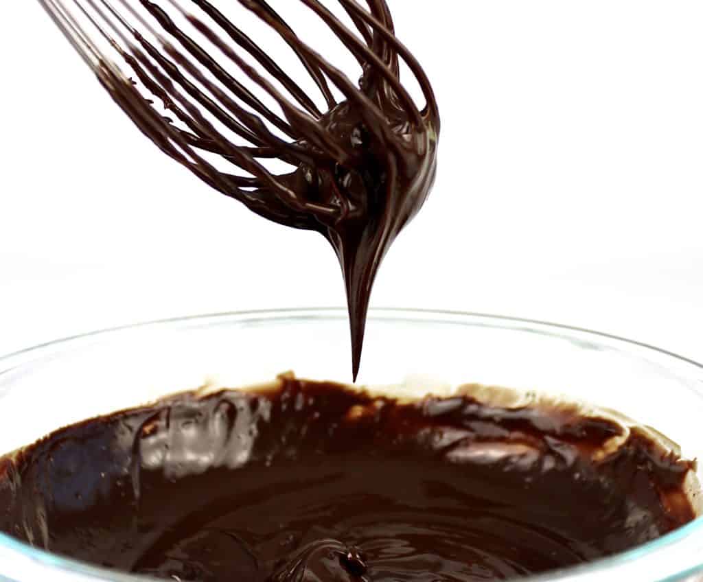 melted chocolate dripping from whisk over glass bowl